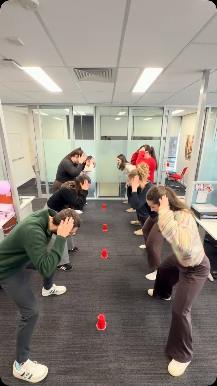 People in an office playing a game with red plastic cups on the floor