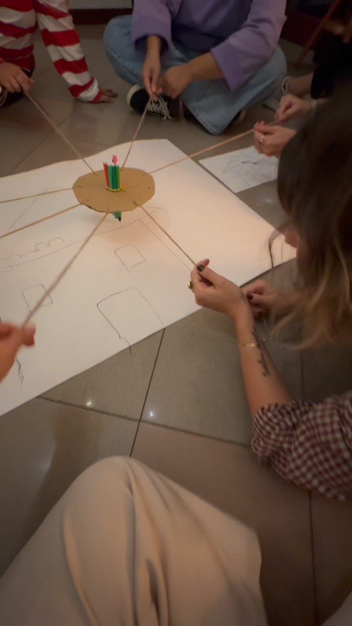 People sitting on a floor playing a team building game with strings and markers.