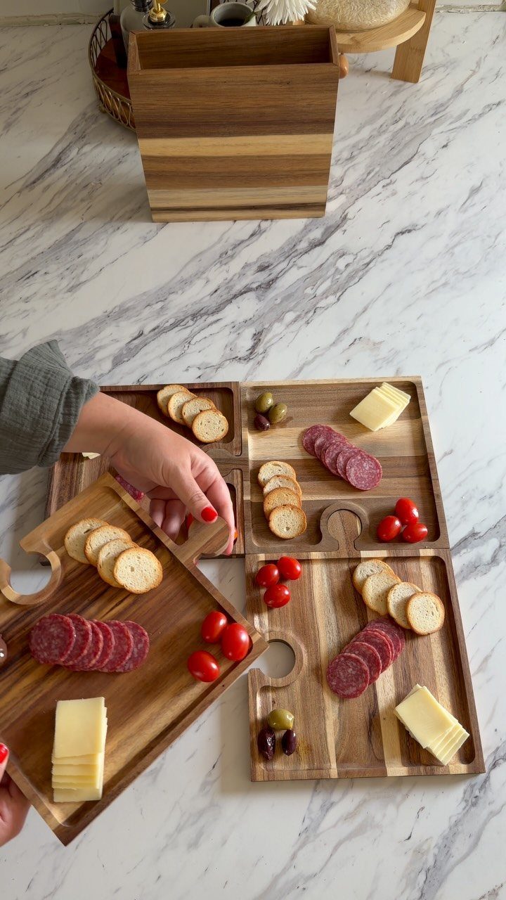 Wooden cheese boards with salami, cheese, crackers, and olives on marble surface