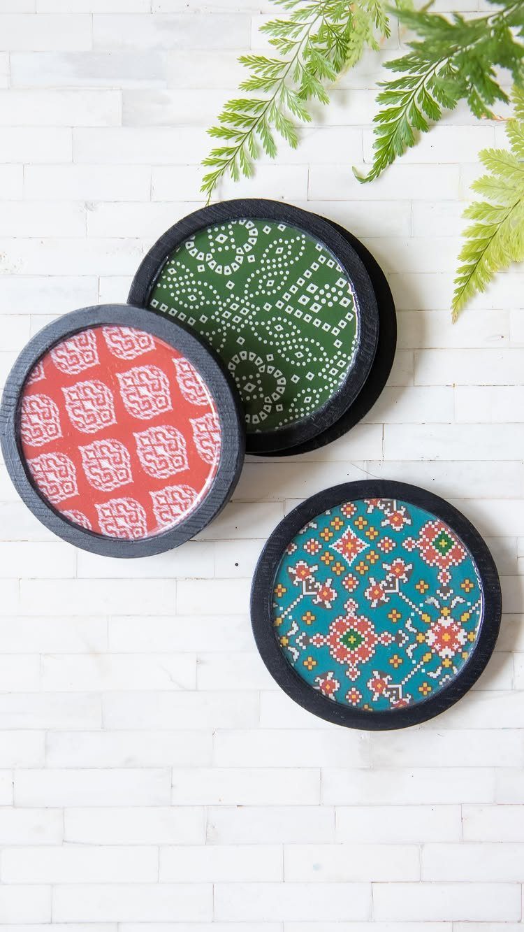 Three round patterned coasters with black rims on a white brick background.