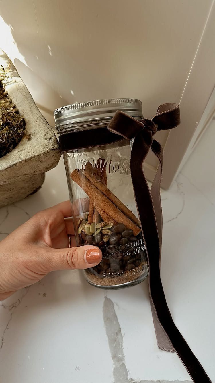 Glass mason jar filled with coffee beans and cinnamon sticks tied with brown ribbon