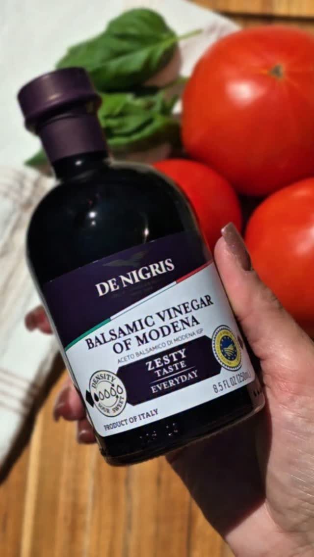 Balsamic vinegar bottle held in hand with tomatoes and basil in background