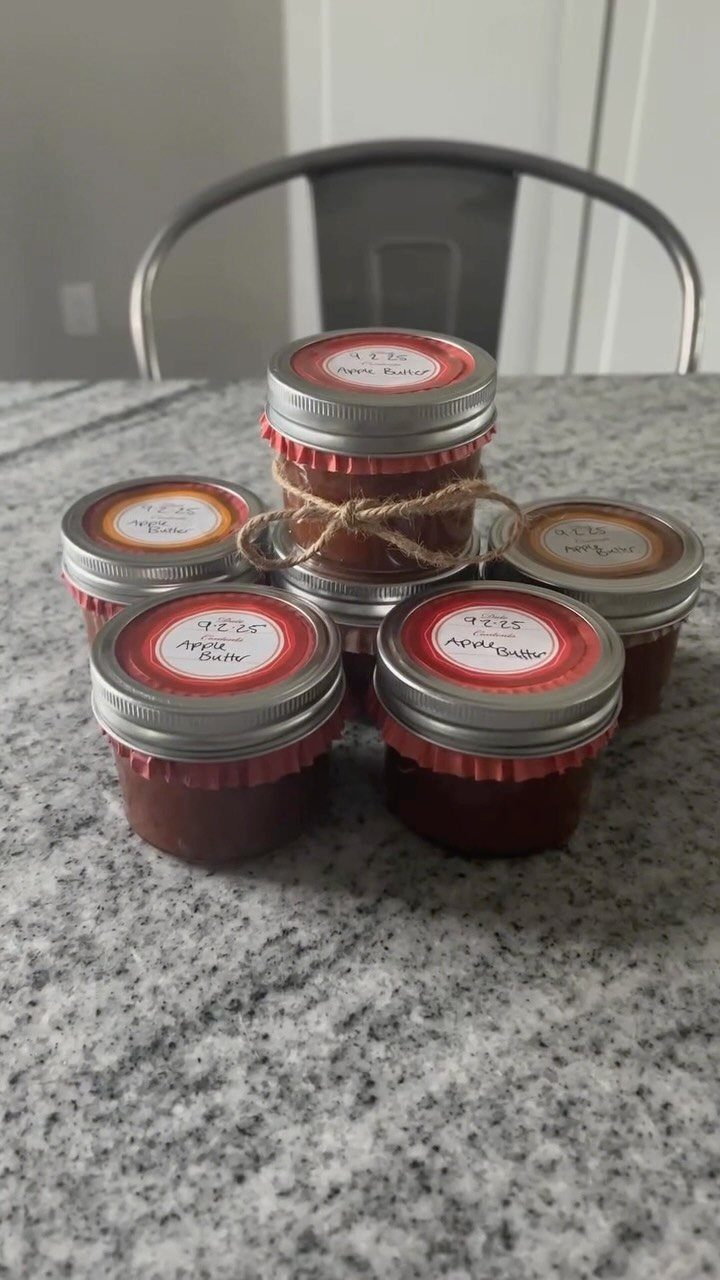 Six small jars of apple butter with red labels on a granite counter