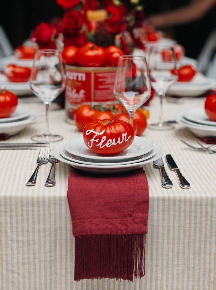 Table setting featuring red tomatoes as decor on plates and in a tin can.