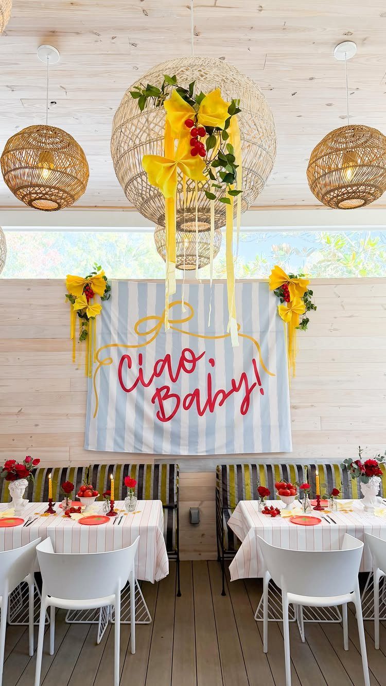 Outdoor party setup with a Ciao Baby backdrop and yellow floral decorations.