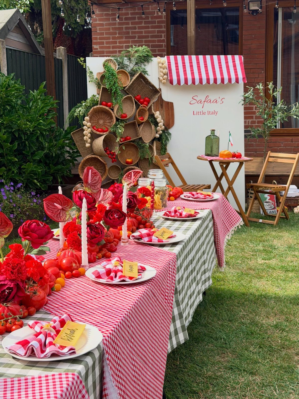 Outdoor Italian party setup with checkered tablecloths, red floral arrangements, and rustic decor.