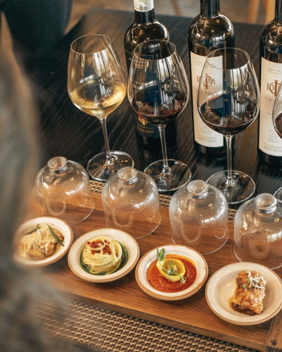Wine glasses and gourmet appetizers on a wooden tray atop a dark table.