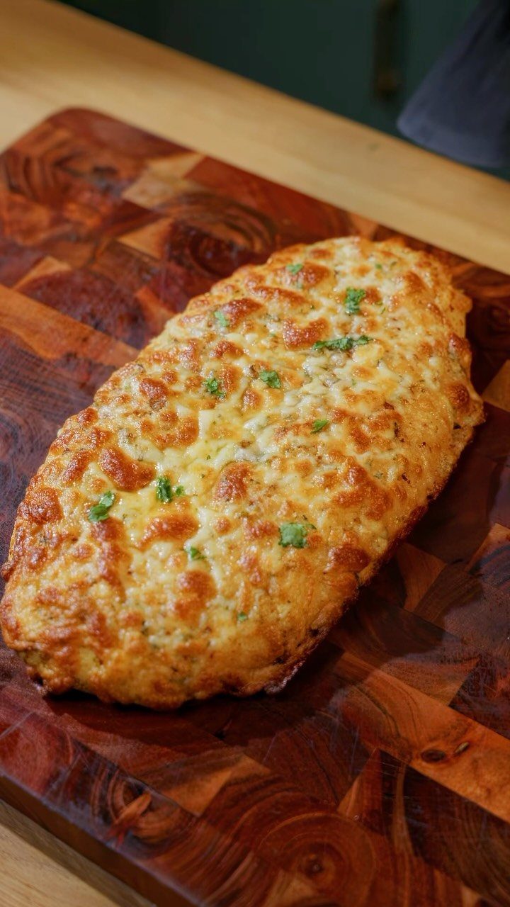 Golden-brown baked cheese bread with herbs on a wooden cutting board.