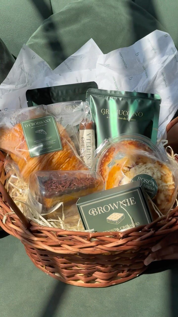 Wicker gift basket filled with packaged croissants, brownies, and cakes in shredded paper.