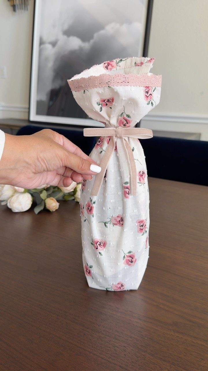 Bottle wrapped in floral fabric with a pink ribbon on a wooden table