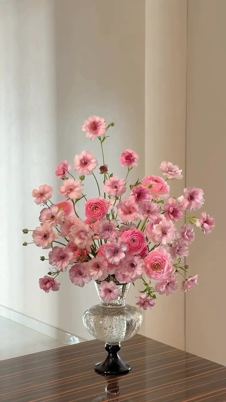 Pink flowers arranged in a textured glass vase on a dark wooden table.