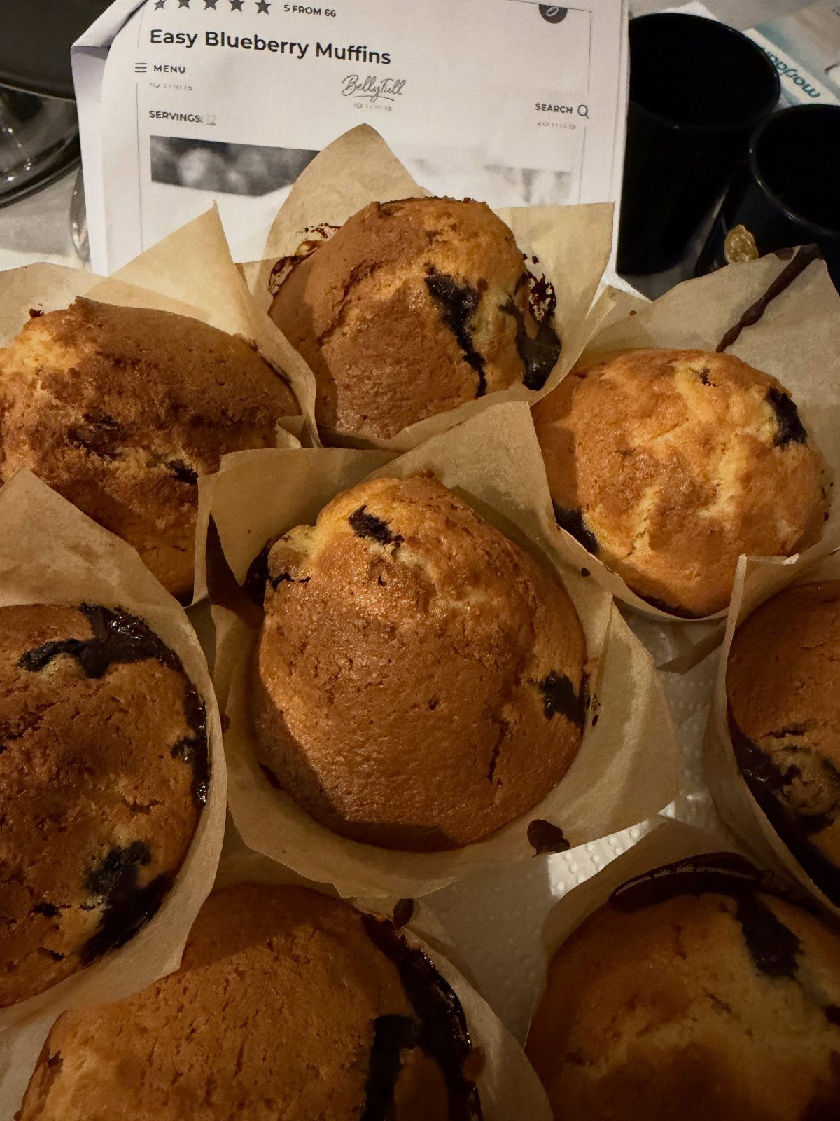 Blueberry muffins in parchment liners with a printed recipe in the background.