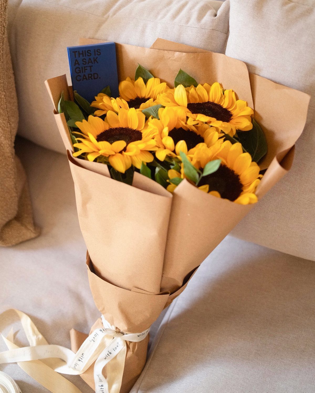 Sunflowers wrapped in brown paper with a small blue gift card tucked inside.