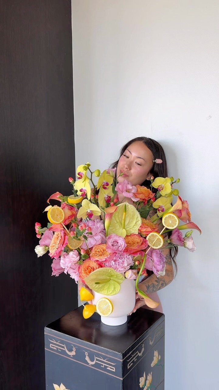 Colorful floral arrangement with pink roses and lemon slices in a white vase.