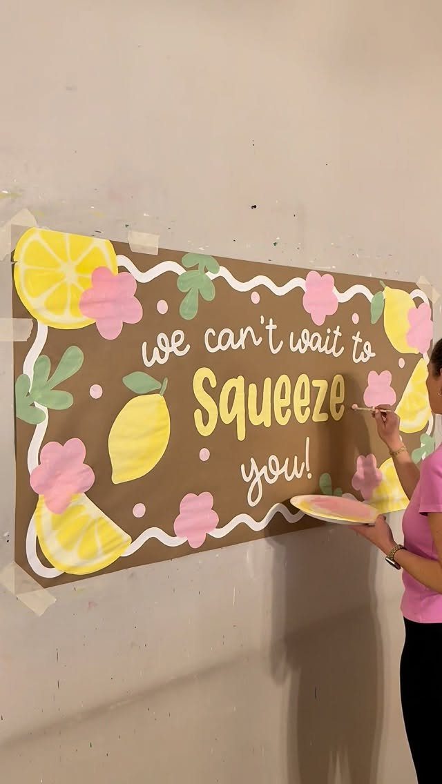 Person painting a lemon themed banner that says we can't wait to squeeze you