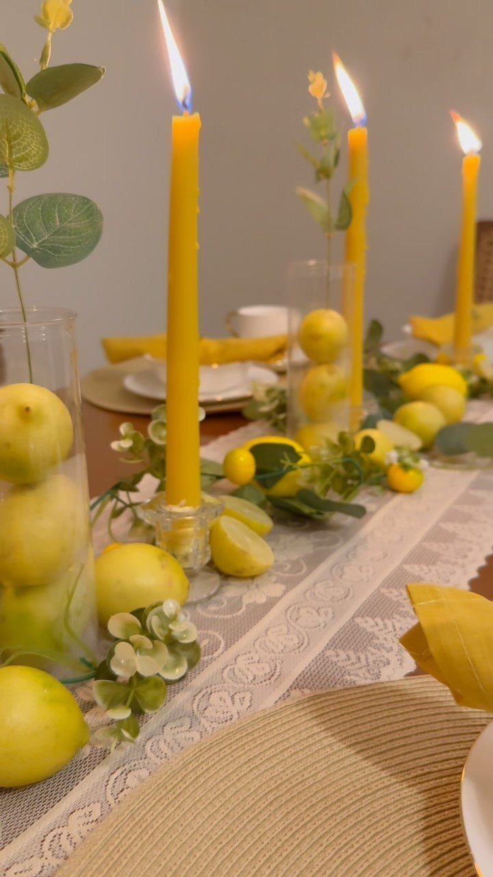 Yellow taper candles and fresh lemons decorating a white lace table runner.