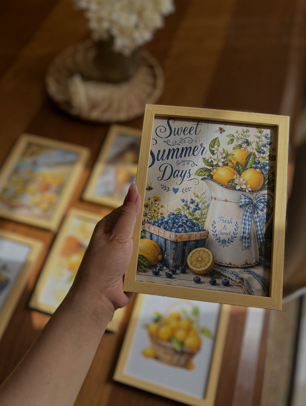 Hand holding a framed art print featuring lemons and blueberries on a table.