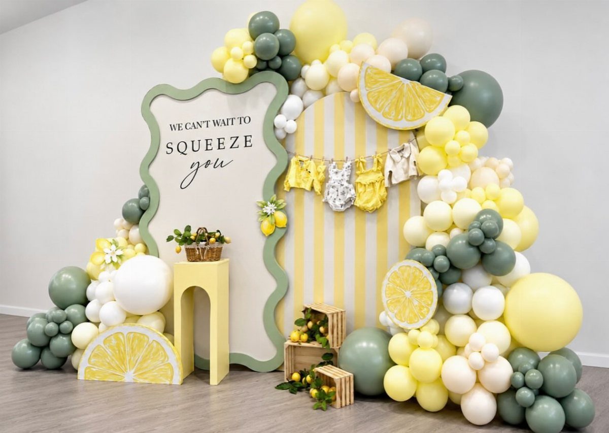 Lemon themed baby shower backdrop with yellow balloons, lemon slices, and baby onesies.