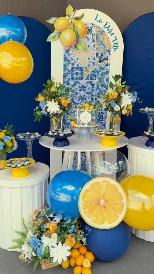 Lemon-themed dessert table with blue and yellow cake stands, balloons, and floral arrangements.