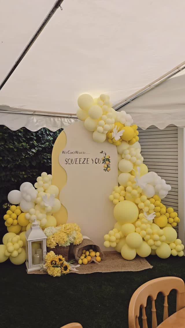 Yellow and white balloon arch backdrop with lemon themed signage and floral arrangements.