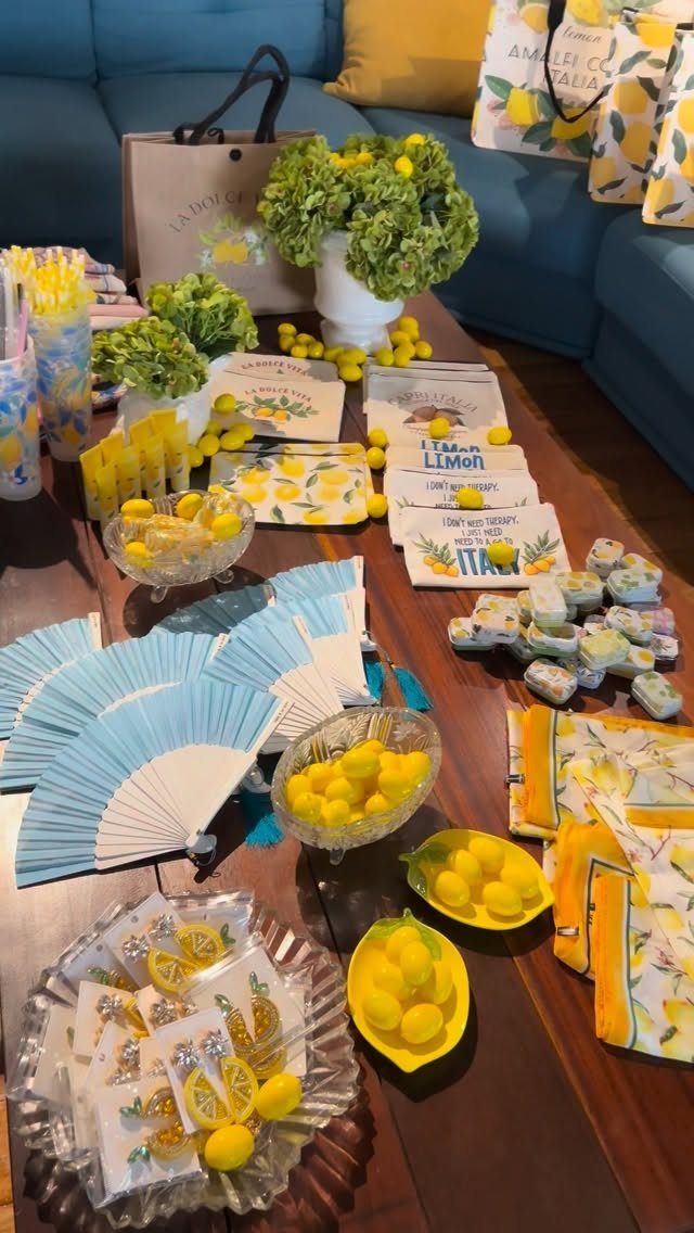 Lemon-themed party supplies including blue fans, yellow candies, and lemon-patterned napkins on table.