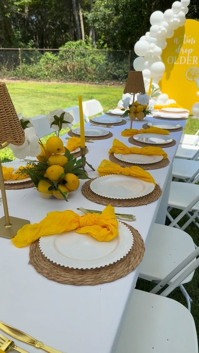 Outdoor party table set with yellow napkins, fresh lemons, and white plates.