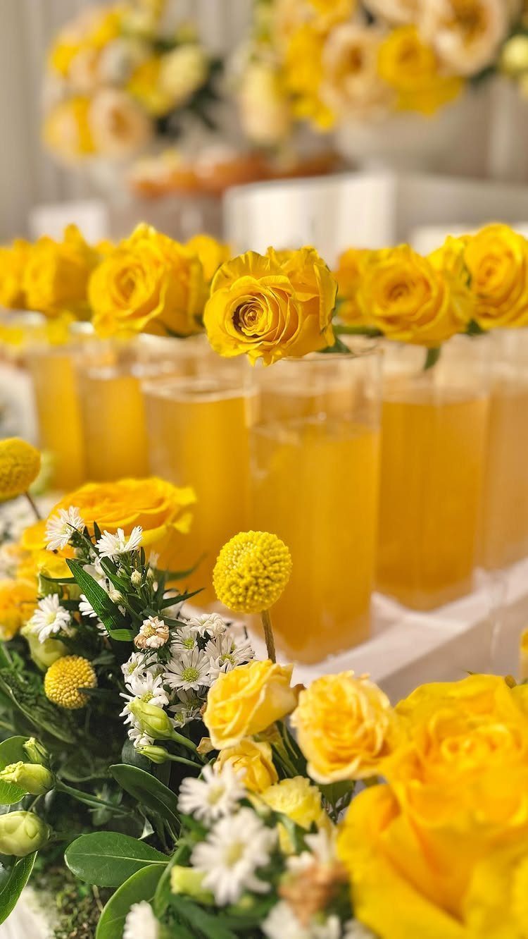 Yellow lemonade glasses topped with roses and surrounded by yellow and white flowers.