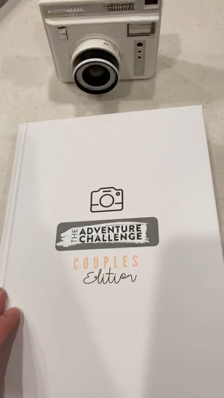 The Adventure Challenge Couples Edition book next to a white instant camera
