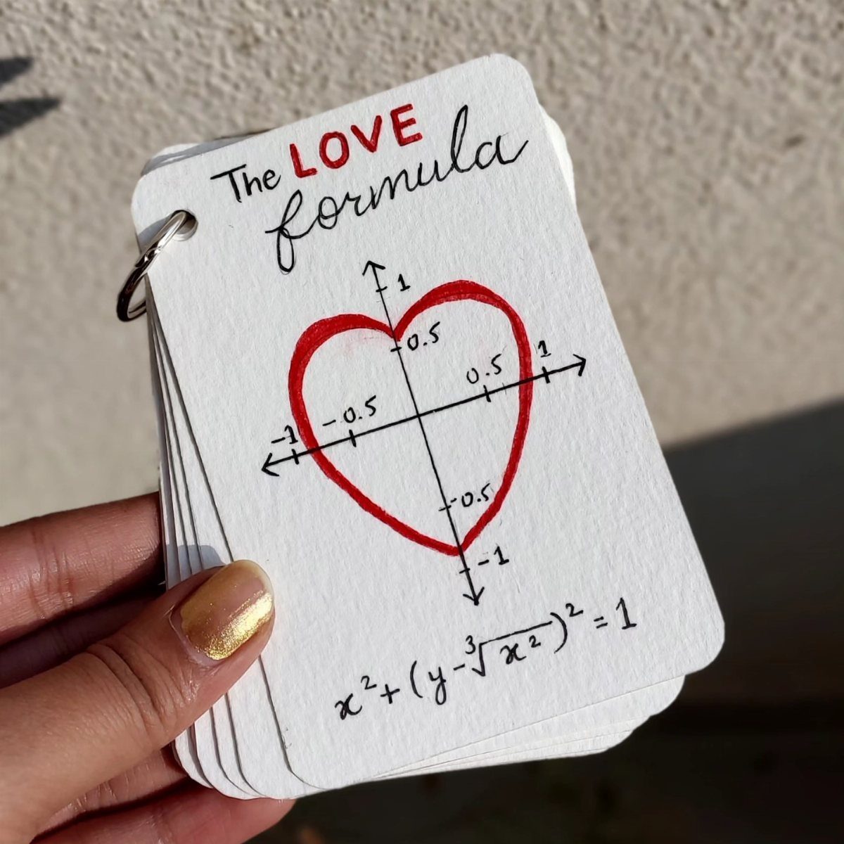 Hand holding a stack of white cards featuring a red heart mathematical formula.