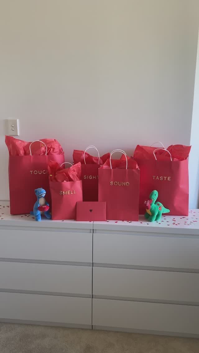 Red gift bags labeled with five senses arranged on a white dresser.