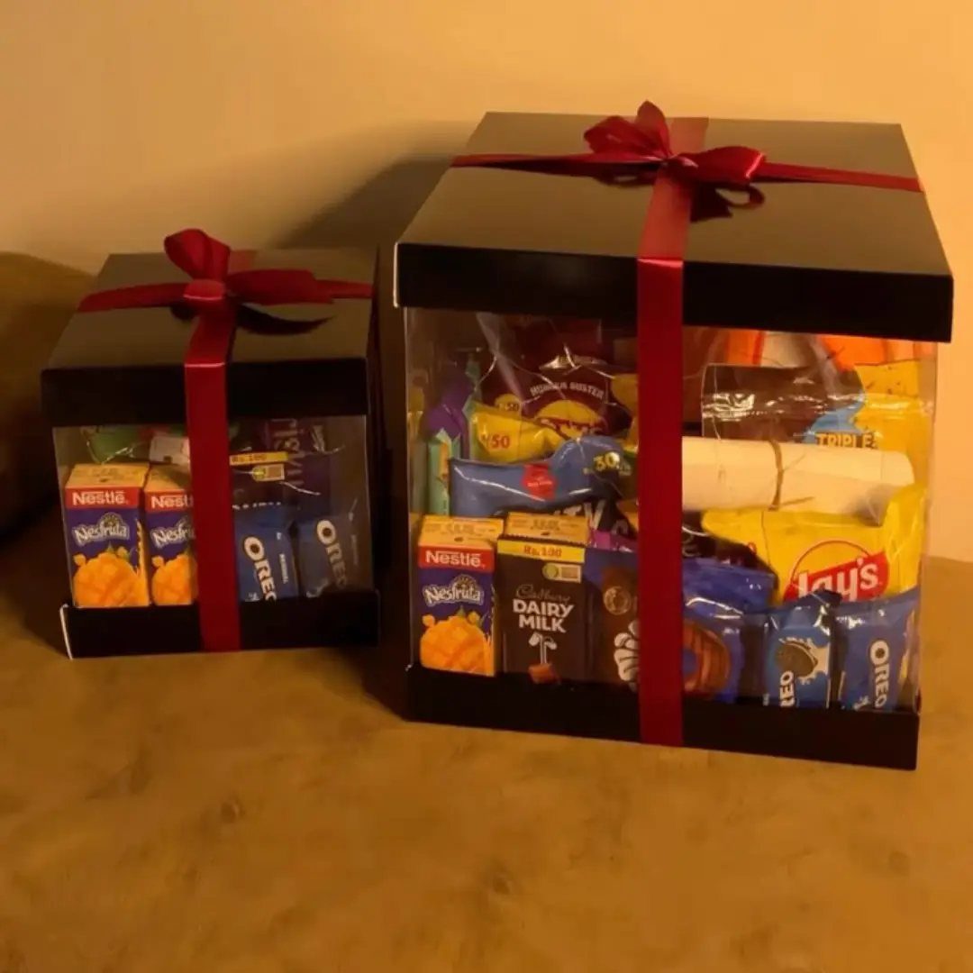 Two black gift boxes with red ribbons filled with assorted chocolates and snacks.