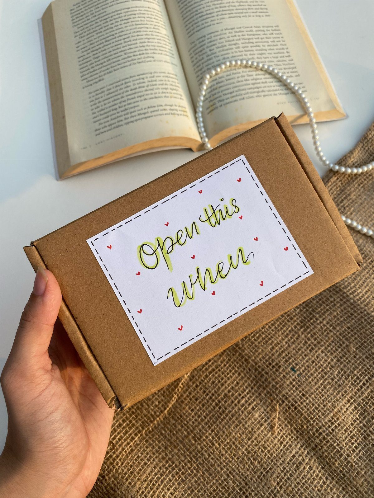 Hand holding a brown gift box with an Open this when label