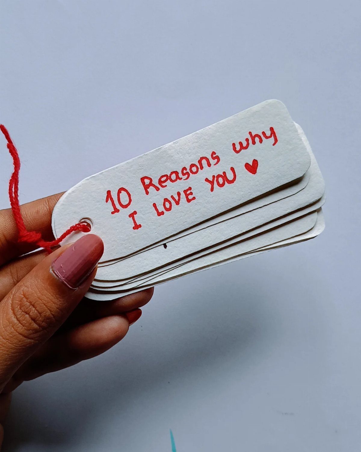 Hand holding a stack of white tags titled 10 Reasons why I LOVE YOU