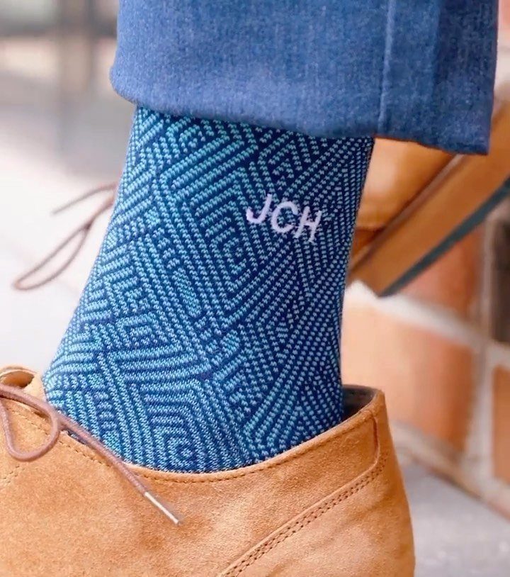 Blue patterned sock with white initials JCH worn with brown suede shoes.