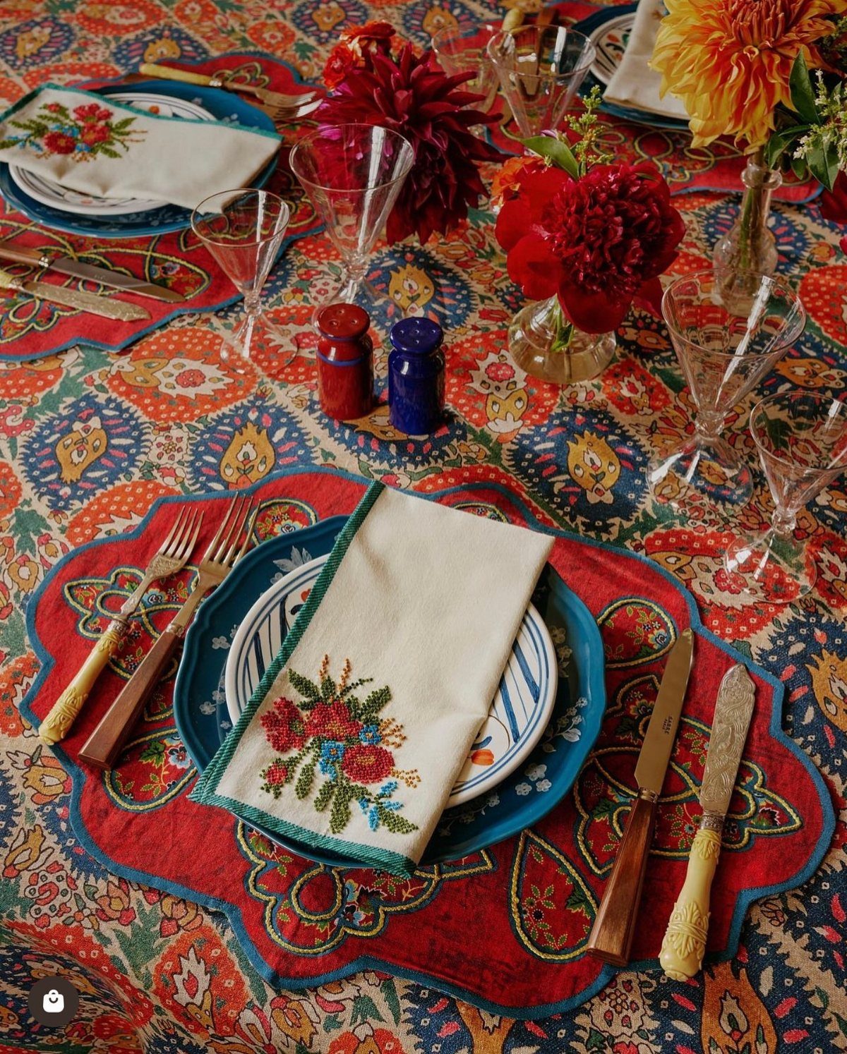 Embroidered white napkins and red placemats on a colorful patterned dining table.