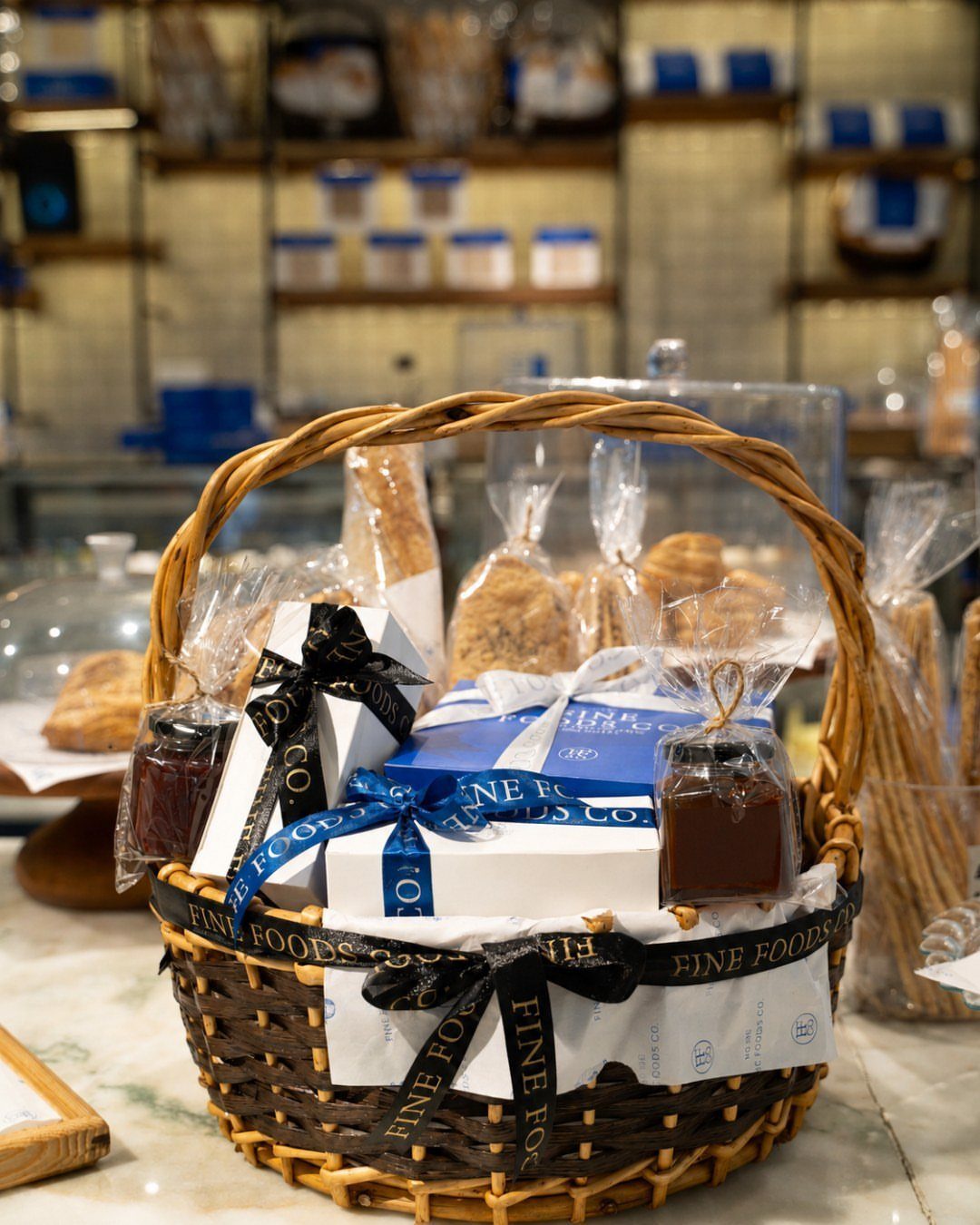 Wicker gift basket filled with gourmet food, ribbons, and packaged treats in a store.