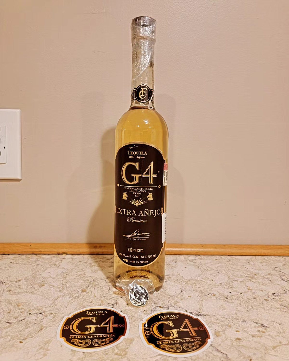 G4 Extra Añejo Tequila bottle standing on a counter with two matching coasters.