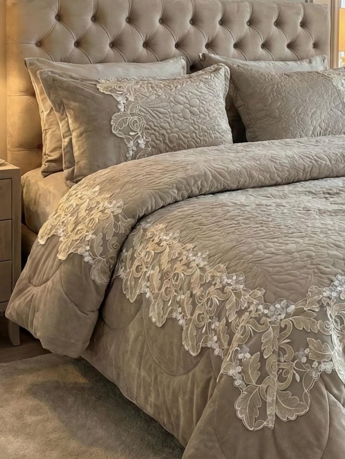 Luxury taupe bedding set with white lace embroidery on a tufted bed.