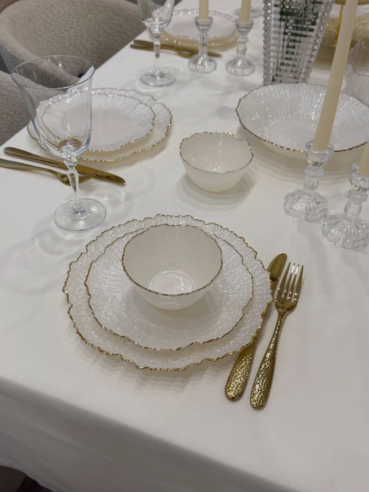 White textured dinnerware with gold rims and gold cutlery on a white tablecloth.