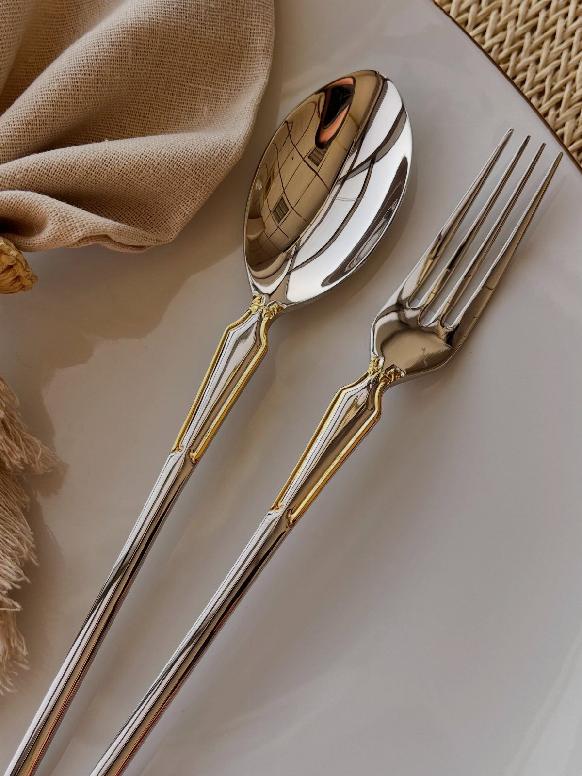 Silver spoon and fork with gold accents on a white plate and napkin.