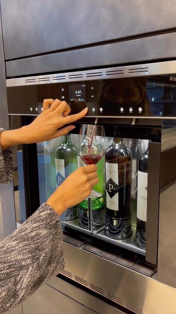 Hands using a built-in luxury wine dispenser to pour red wine into a glass.