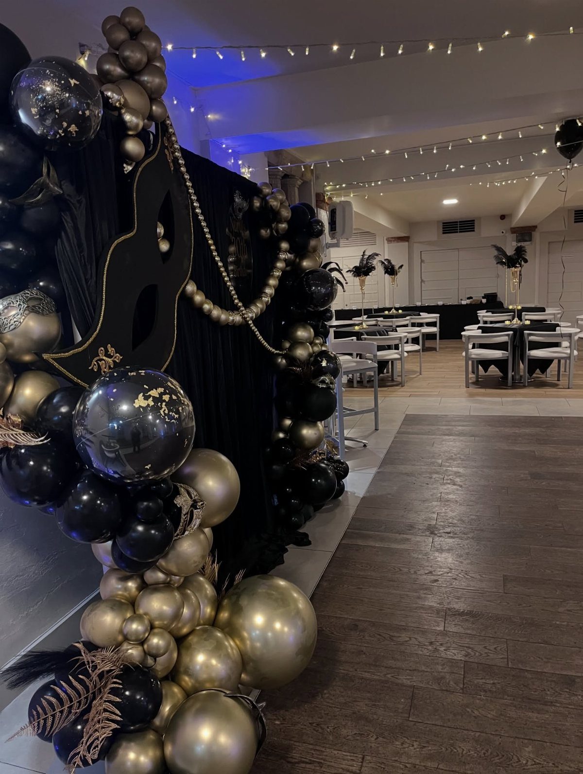 Black and gold balloon arch with a large mask silhouette for a party.