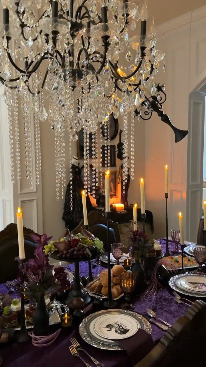 Elegant dining table with purple linens, white candles, and a crystal chandelier above.