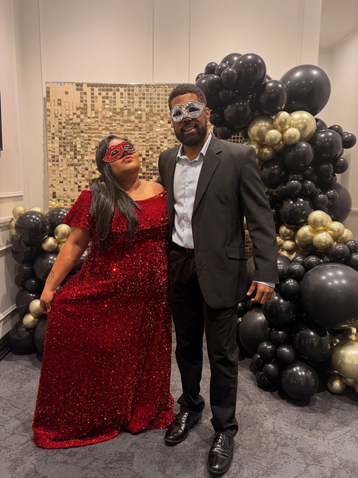 Couple in masquerade attire wearing masks, a red gown, and a black suit.