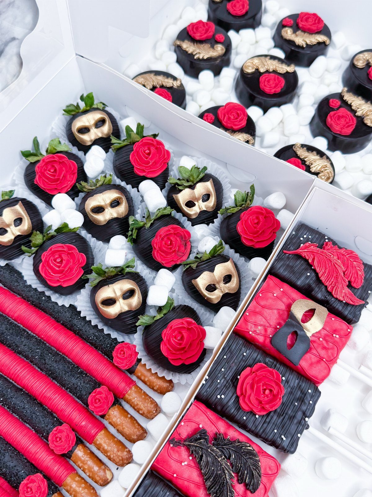 Chocolate-covered strawberries and desserts decorated with red roses and gold masquerade masks.