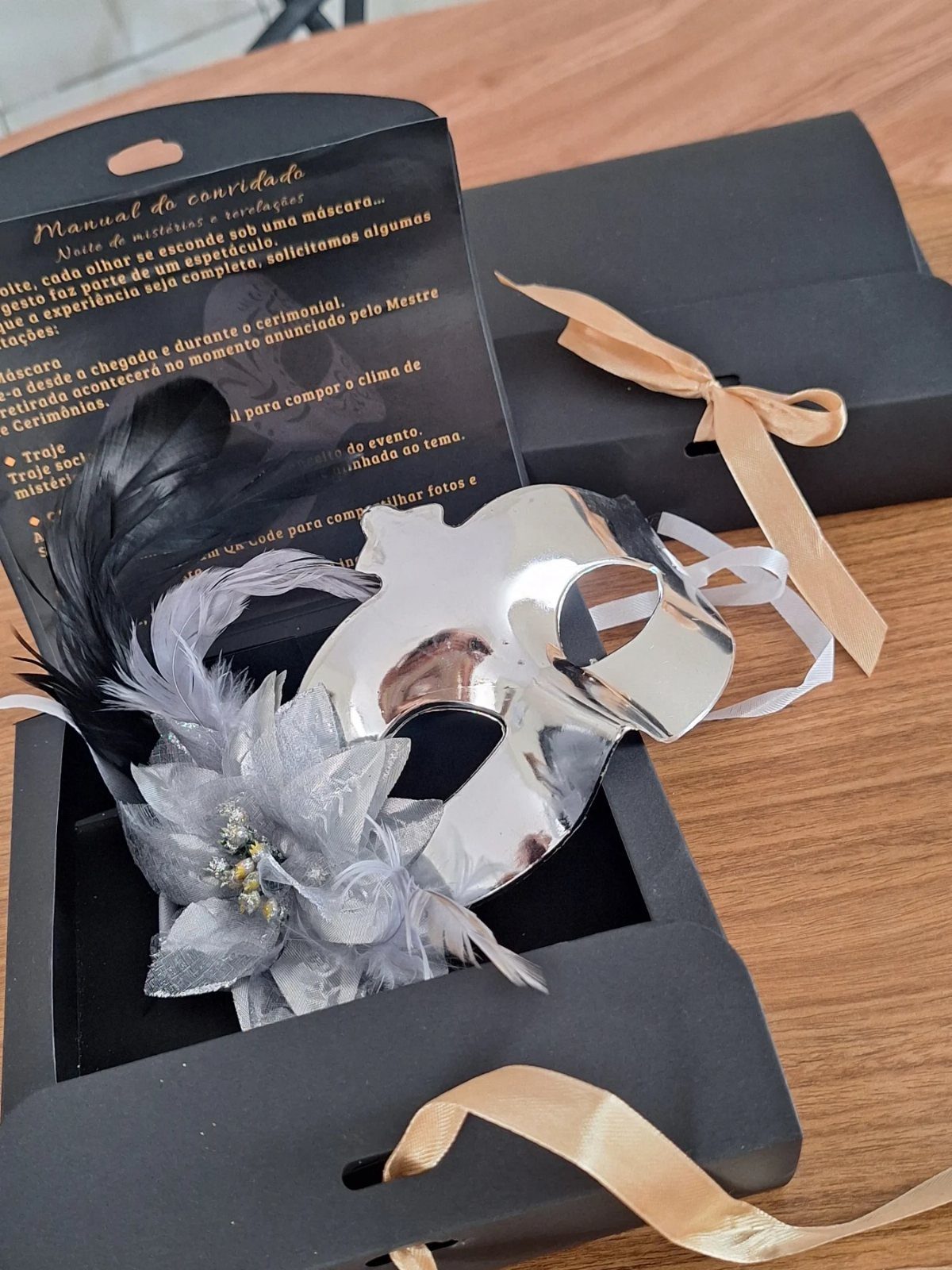 Silver masquerade mask with feathers and flower in a black gift box