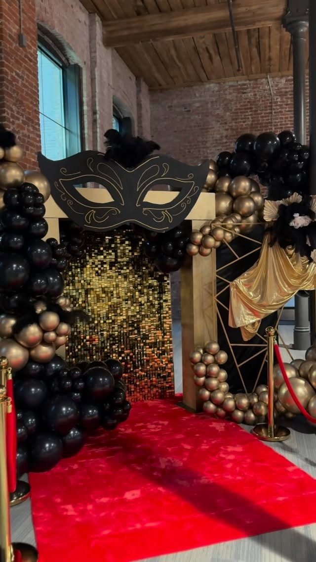 Red carpet entrance with black and gold balloons and a large mask cutout.