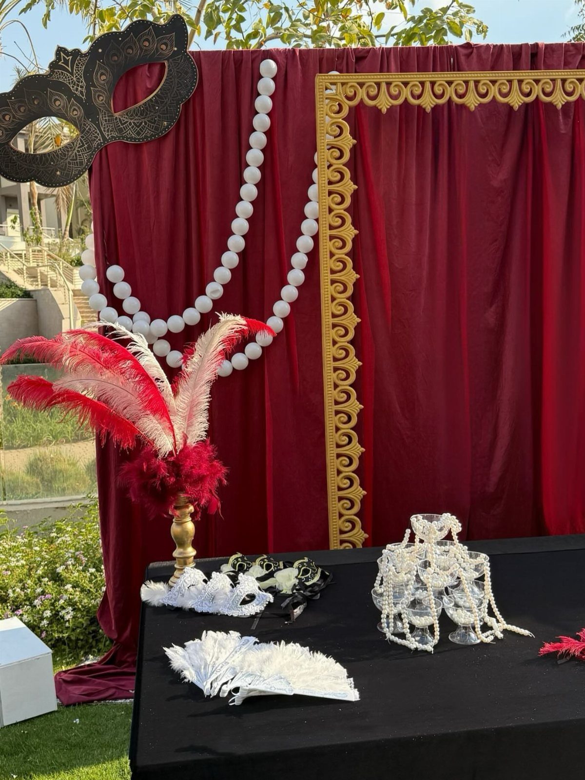 Masquerade party setup with red velvet curtains, gold frame, and lace masks.