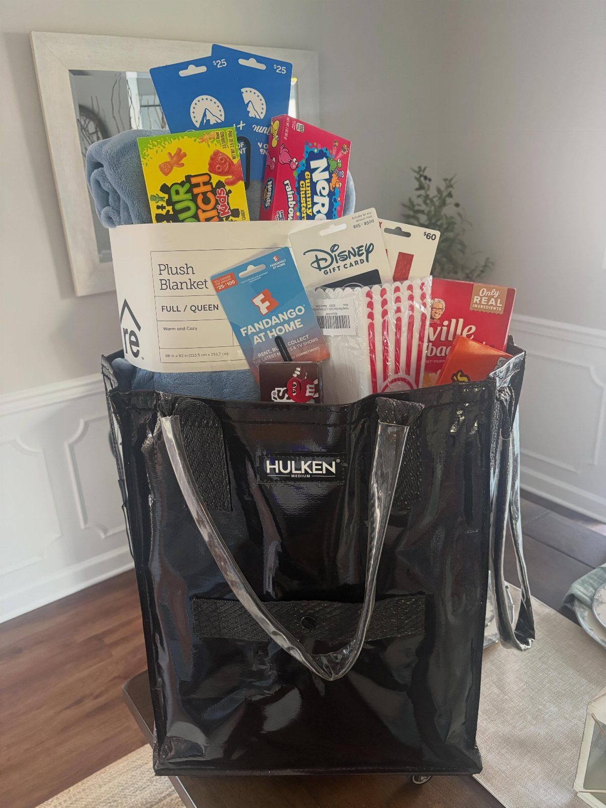 Black glossy tote bag filled with movie snacks, gift cards, and a blanket.
