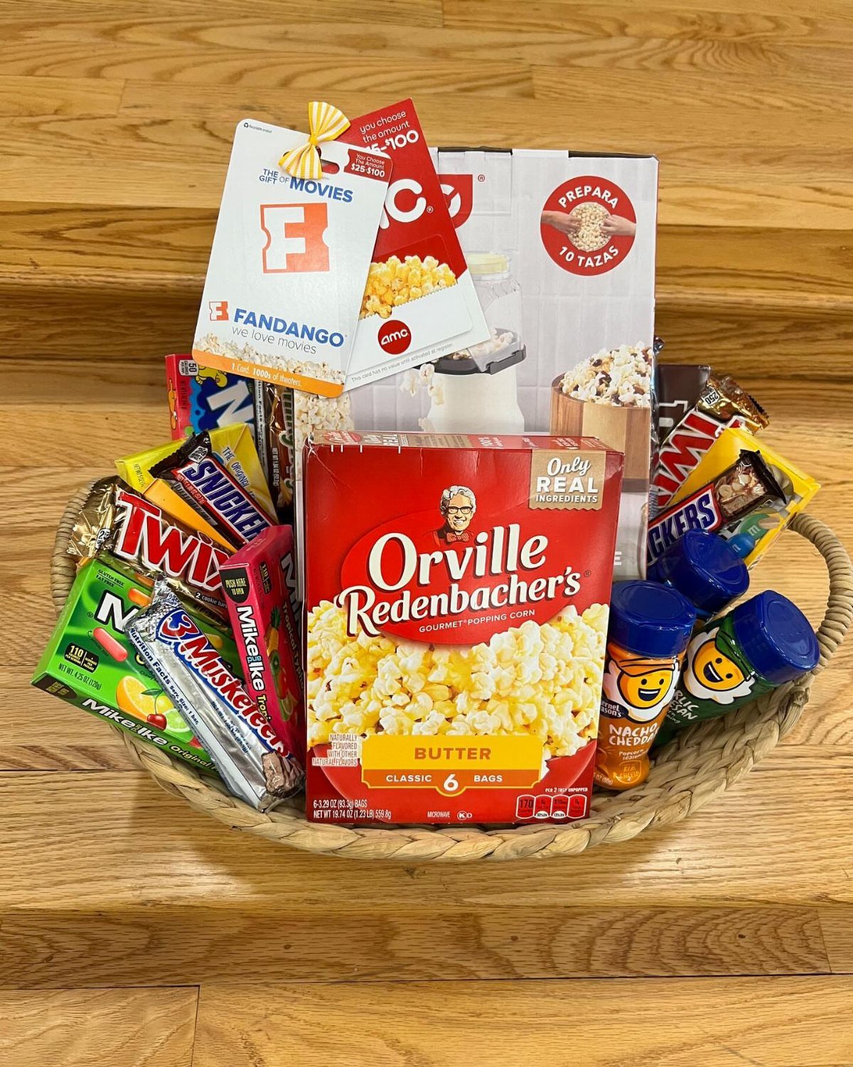 Wicker gift basket filled with popcorn, assorted chocolate candies, and a movie gift card.